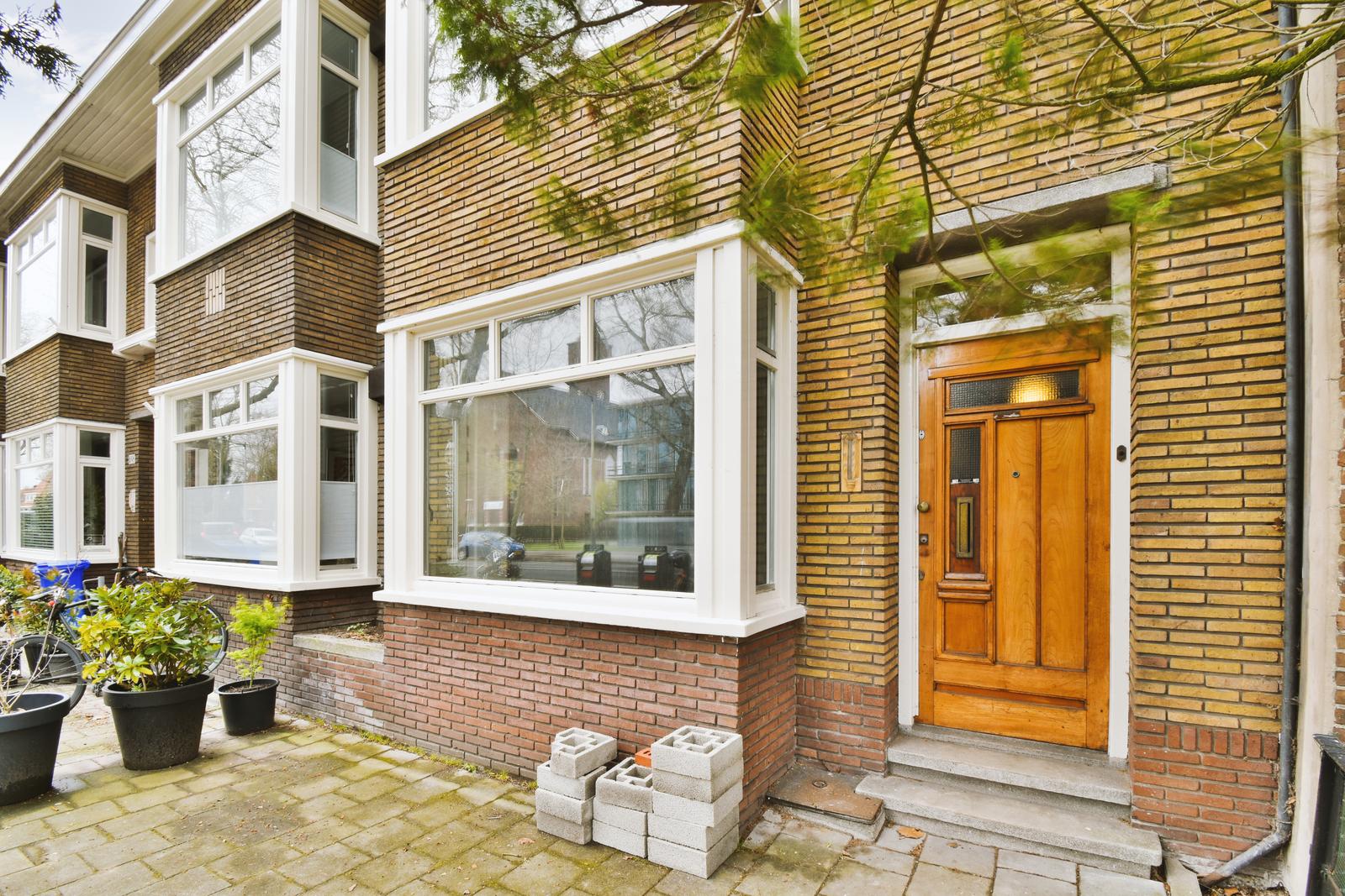 The front view of a brick building with signs, pavement and wooden doors lead to the apartment